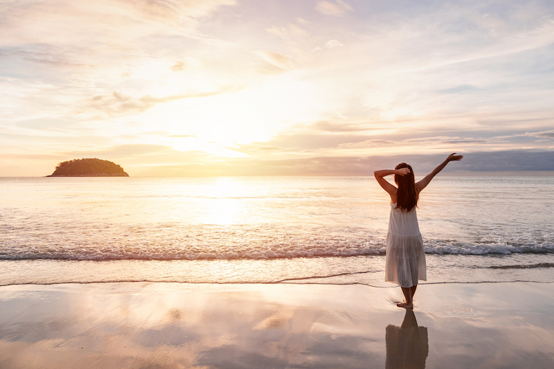Young woman walking and enjoying beautiful Sunset on the tranquil beach.