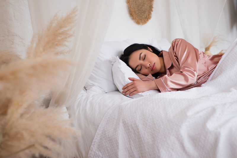 Woman in silk pajamas peacefully sleeping in bed with white linen in bedroom