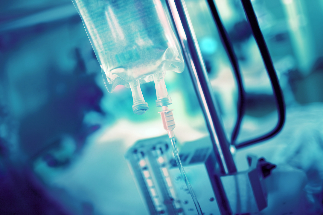 IV drip on the background of blurred hospital equipment and patient in the bed.