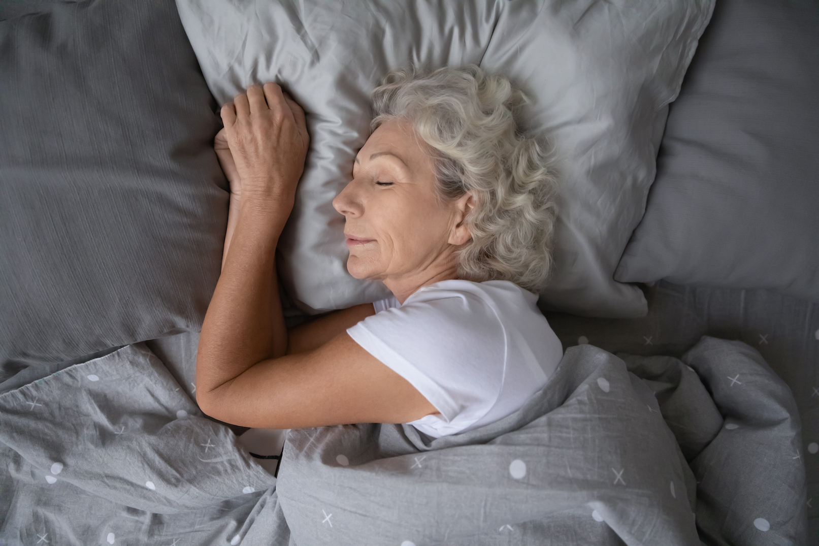 Above top view calm peaceful elderly mature hoary woman sleeping on soft pillow under blanket, illustrating the importance of deep sleep