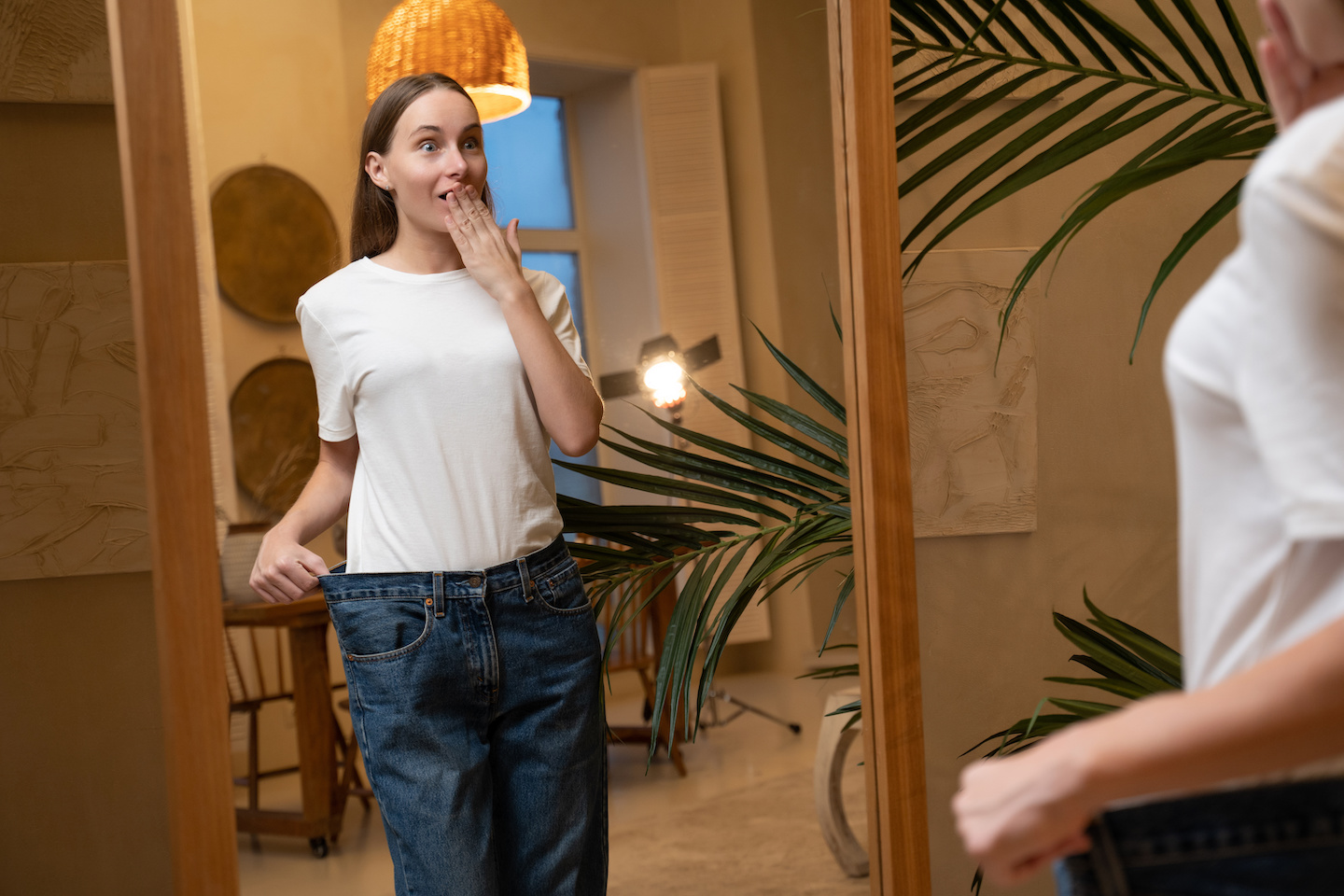 A woman who has lost a lot of weight due to a diet looks in the mirror and shows big jeans.