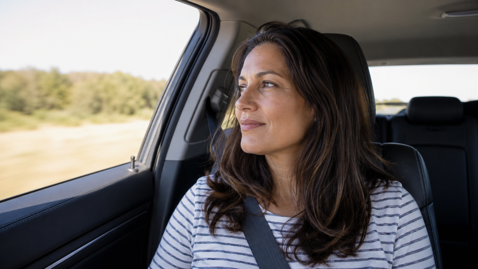 A relaxed adult with a seatbelt on gazing calmly out the car window while being driven home after a ketamine session.